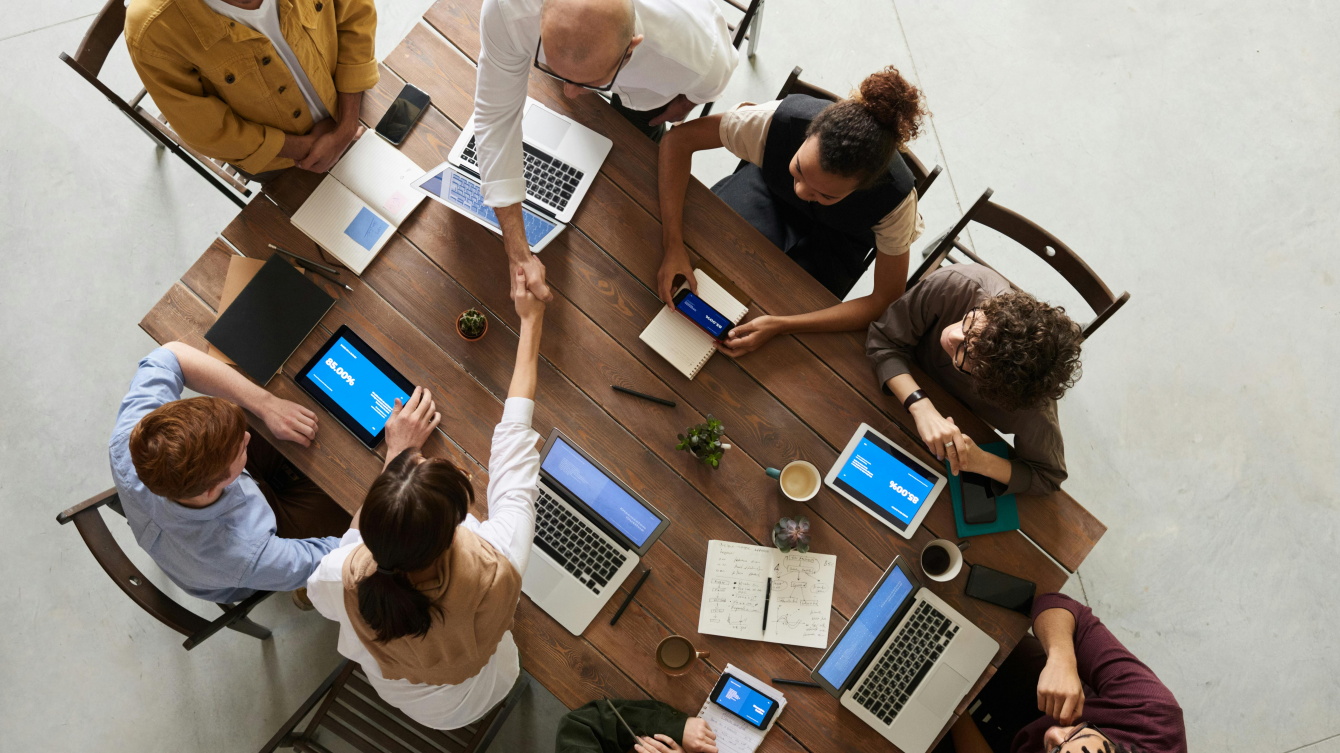 Personas alrededor de una mesa con ordenadores, y dos de ellas se dan la mano