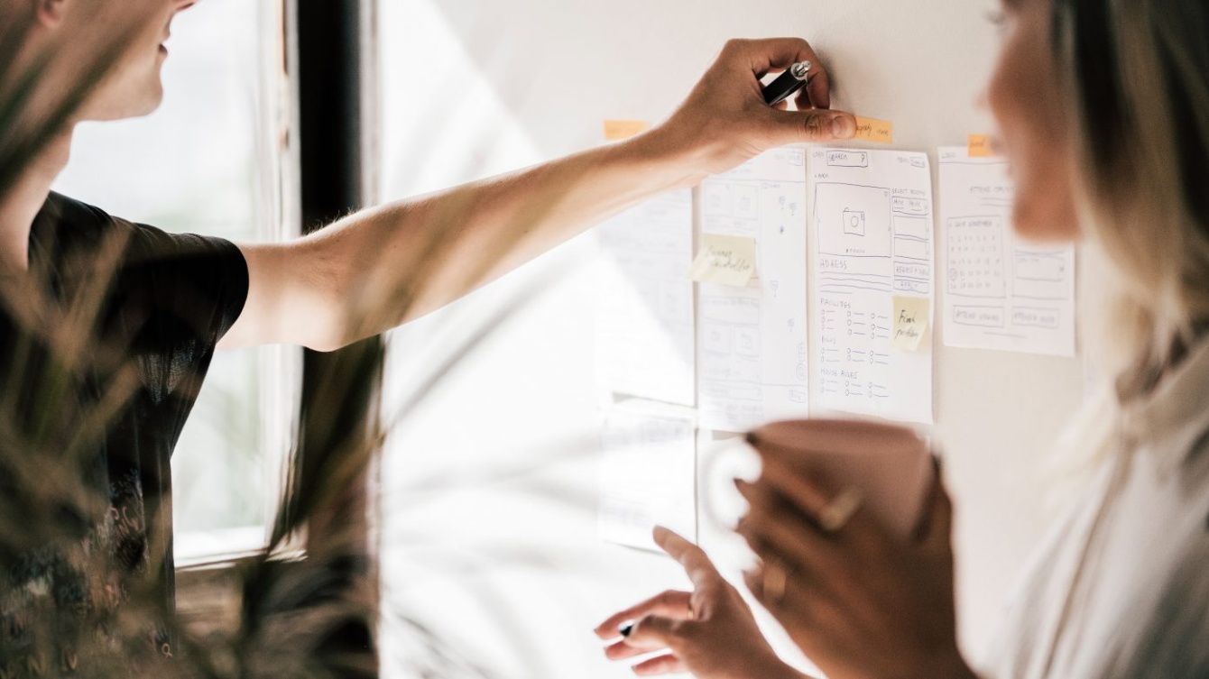 Un hombre y una mujer colocan folios en una pared 