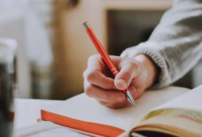 Koaderno batean boligrafo batekin idaztear dagoen gizon baten besoa