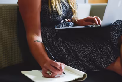 Mujer sentada con un ordenador portátil y escribiendo en un cuaderno